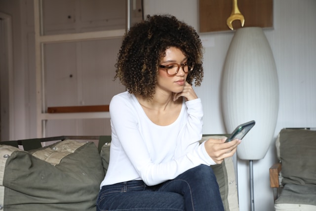 Person som sitter i soffan och jämför mobilabonnemang på sin telefon